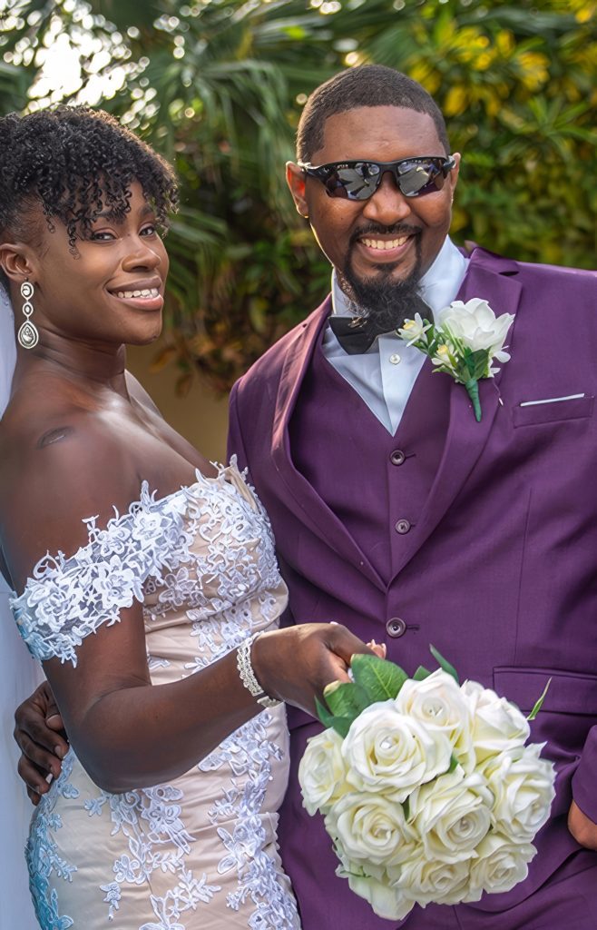 Smiling bride and groom in purple suit holding a white bouquet